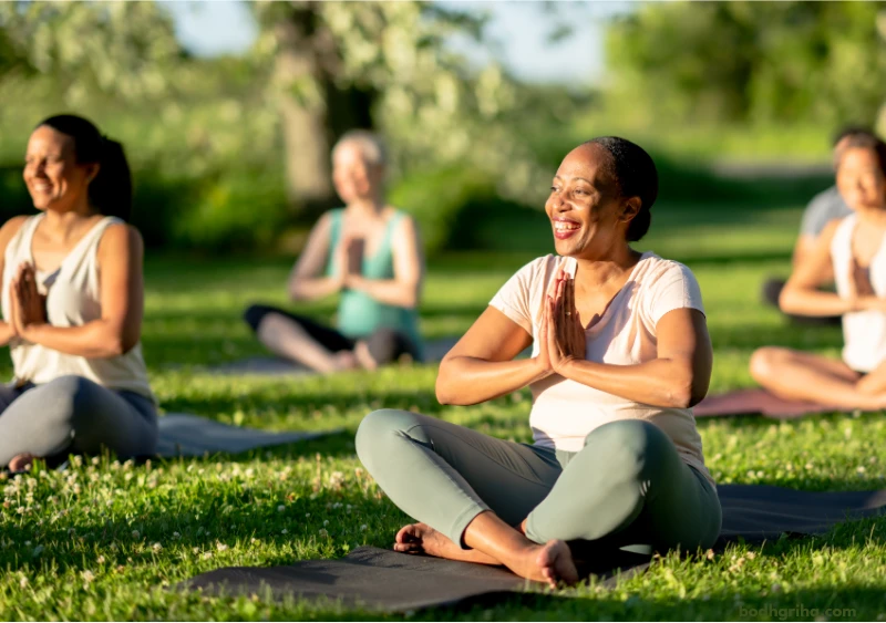 several women are sitting on mats in a park doing